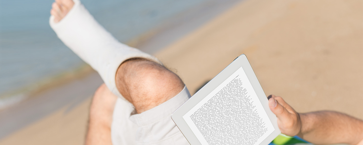 Mann mit Gips liest E-Book am Strand